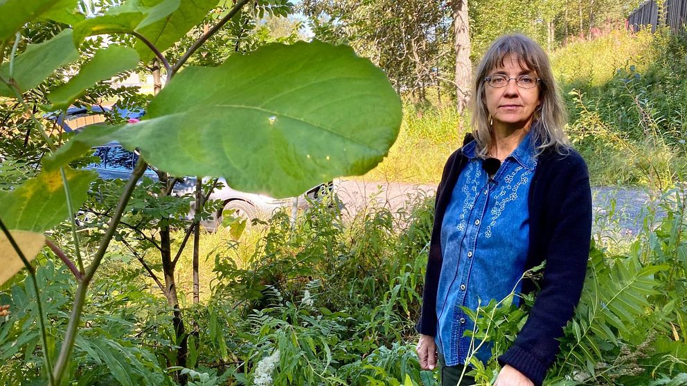Lena Bondestad – en medelålders kvinna – står bland grön växtlighet vid sidan av en grusväg