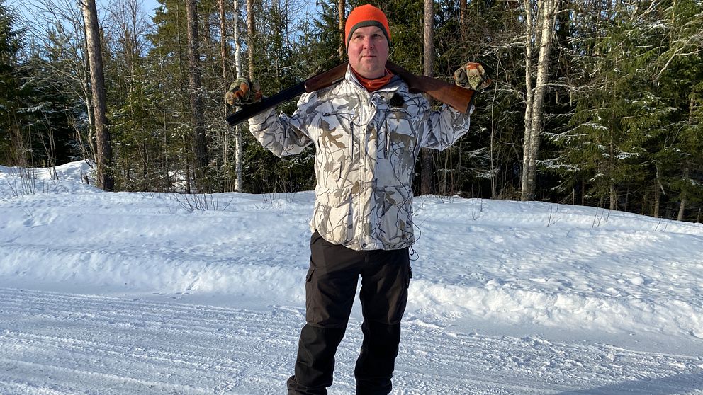 Jägaren Anders Gravsjö i Rättvik står mitt i bild med geväret vilande över axlarna. I bakgrunden står träd och marken är snöig.