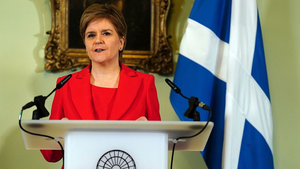 Nicola Sturgeon står vid ett podium med mikrofoner. Till höger Skottlands flagga.