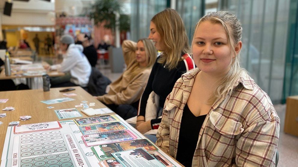 Studenten Kjerstin Dalbert sitter inne i Karlstads universitets byggnad med andra studenter runtomkring sig.