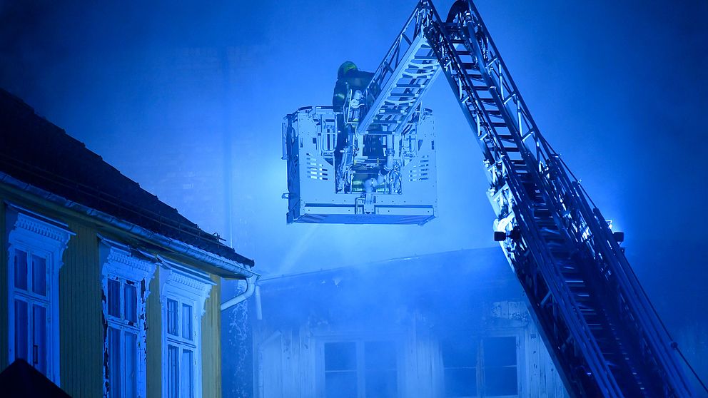 En brandman i korgen till en kranbil vid ett hus som ryker.