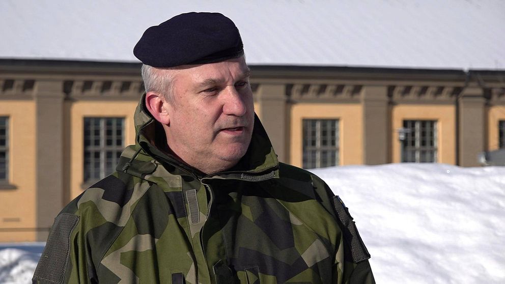 Man i militärkläder står utomhus. Det är snö och i bakgrunden syns en gulbrun byggnad.
