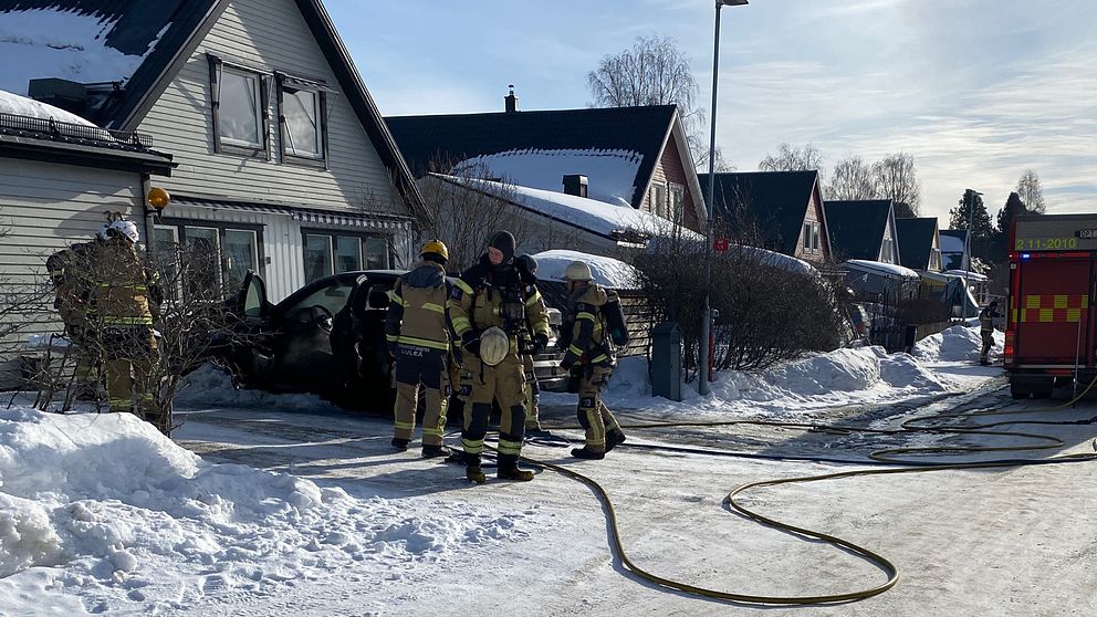 Ett gäng brandmän står och observerar den nedbrunna bilen utanför ett hus på Hertsön.