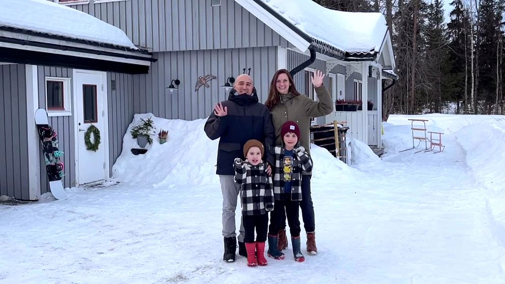 en familj med en pappa, en mamma och två barn, som står i vinterkläder i snön utanför sitt hus i Malå, de vinkar och ser glada ut