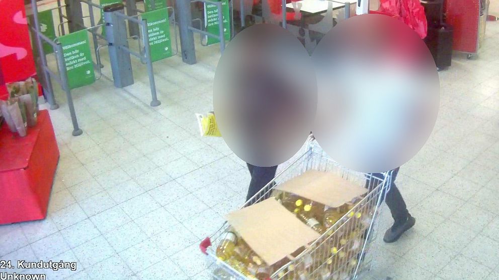 Blurrad bild inifrån en matvarubutik. Två personer går med en kundvagn full med rapsolja. Båda personerna är blurrade.