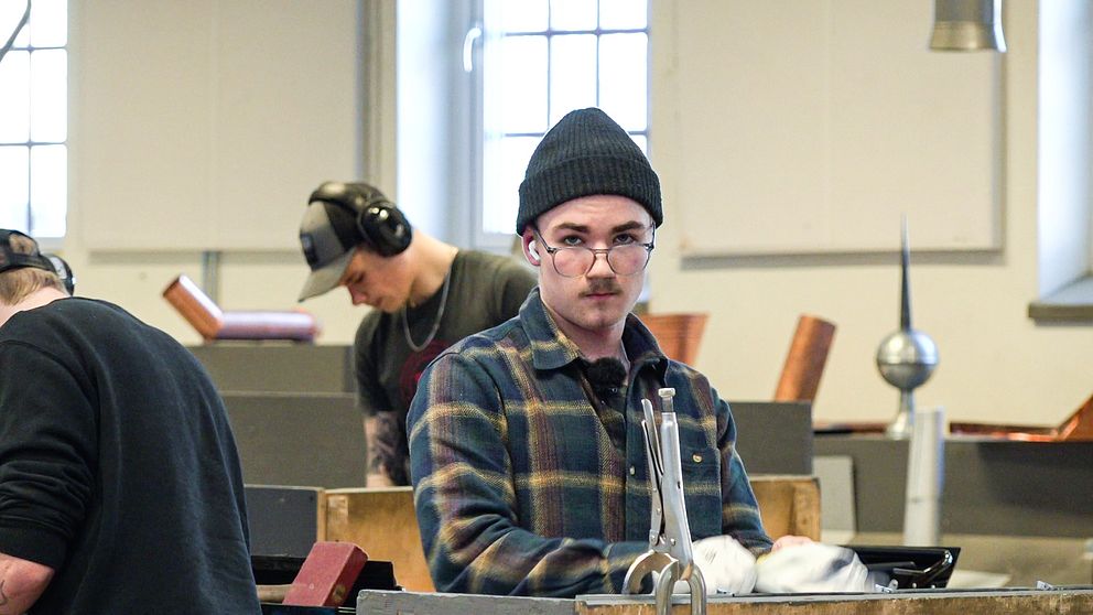 En kille i glasögon och mössa som heter Tor Lundström står vid en arbetsbänk.