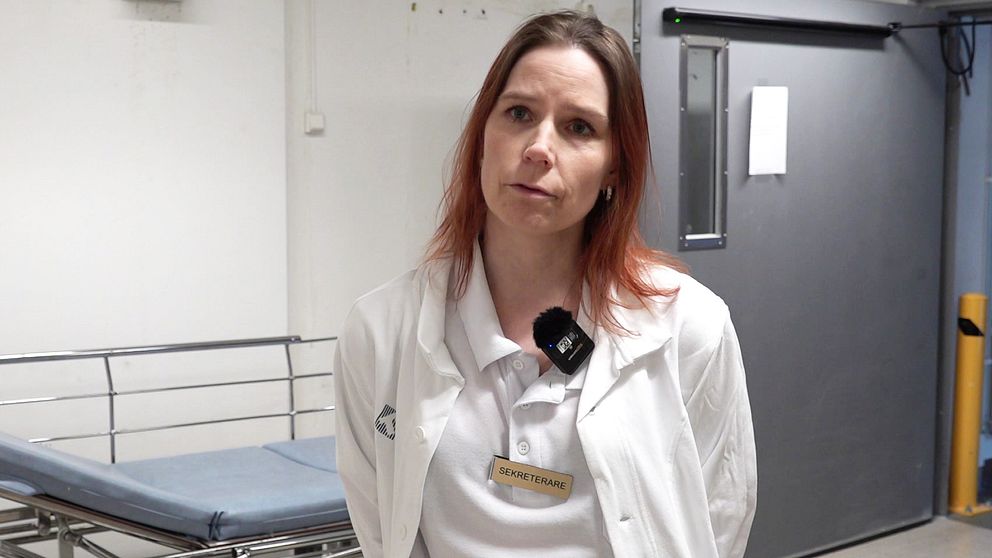 Anna Nilsson står framför sjukhussäng i vita arbetskläder. Har rödbrunt hår.