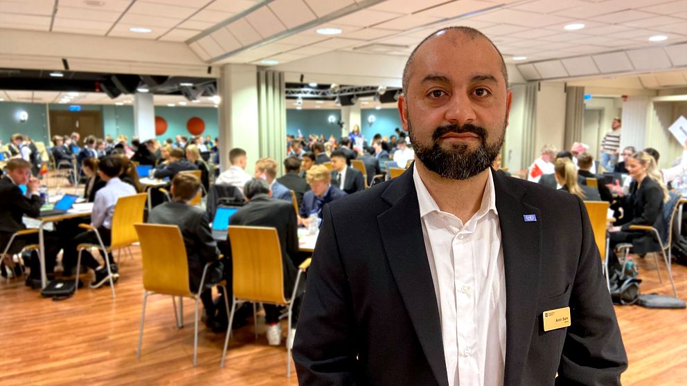 En man står framför ett stort rum med ungdomar som genomför ett FN-rollspel