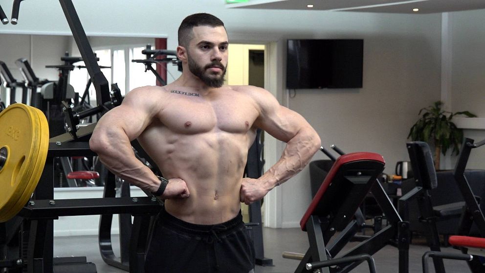 En ung man med muskulös kropp i bar överkropp i gymmiljö.
