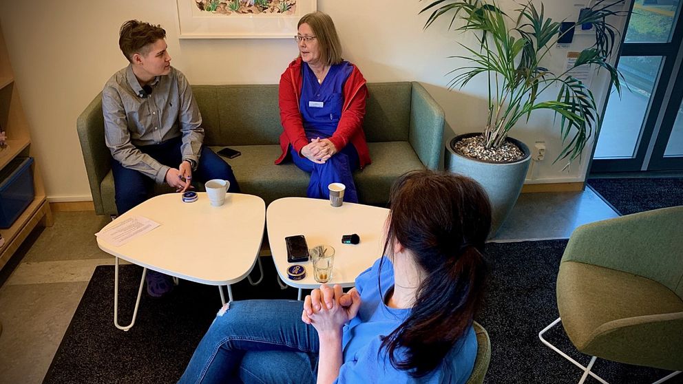 En ung kille i grå skjorta sitter och pratar med en vårdpersonal som bär regionens blå arbetskläder. Mittemot dem sitter Kajsa Sjöberg i blå tröja hon är vårdenhetschef.