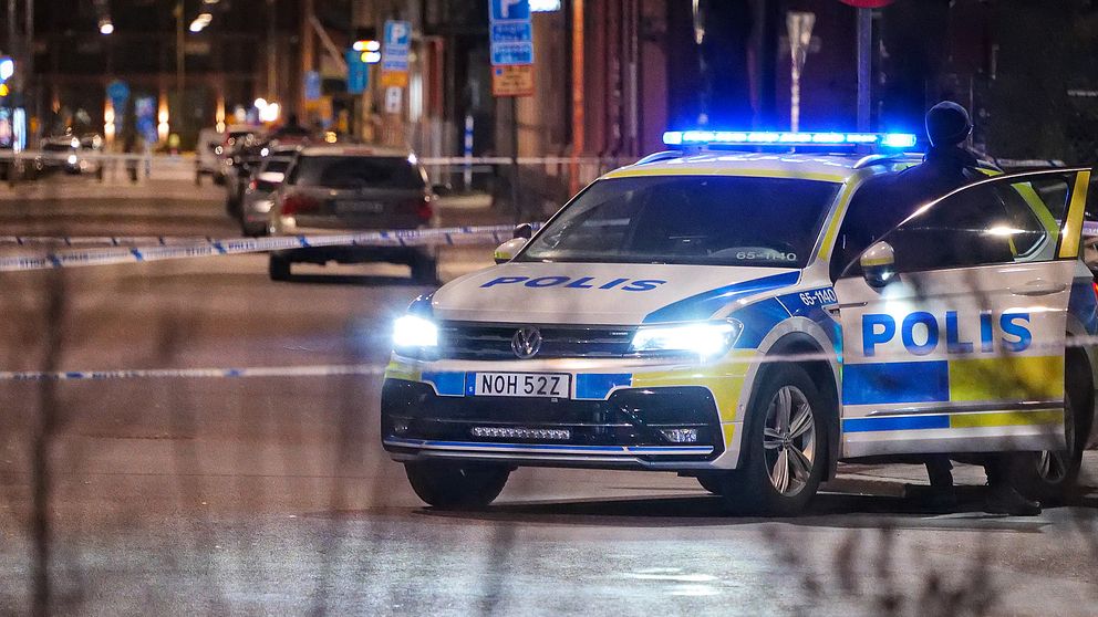 En bild på en polisbil som står innanför polisavspärrningar på en gata.