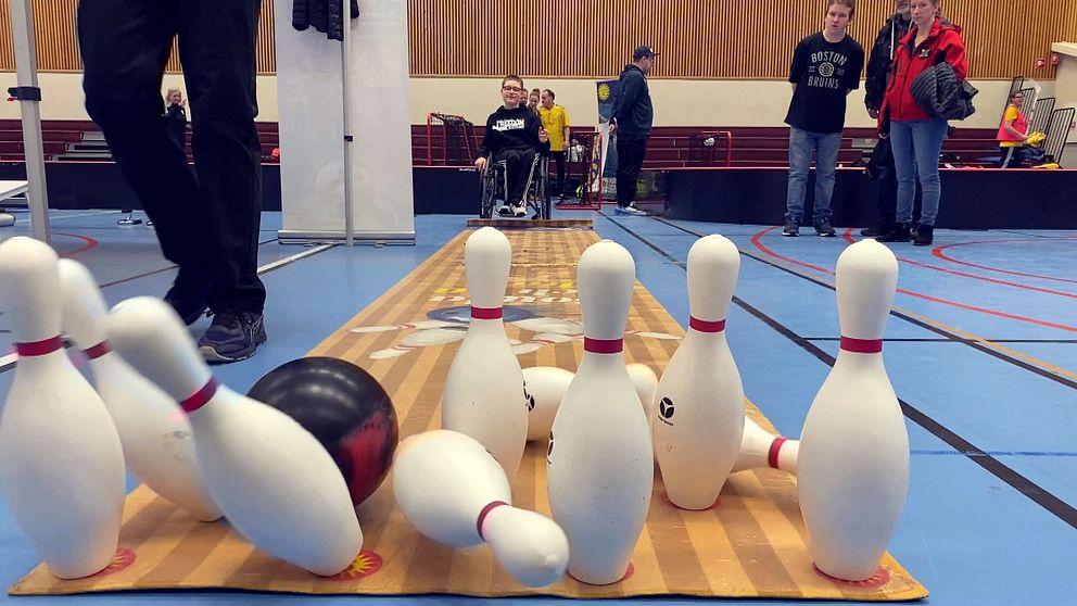 Pojke i rullstol har kastat ett bowlingklot som fäller flera käglor.