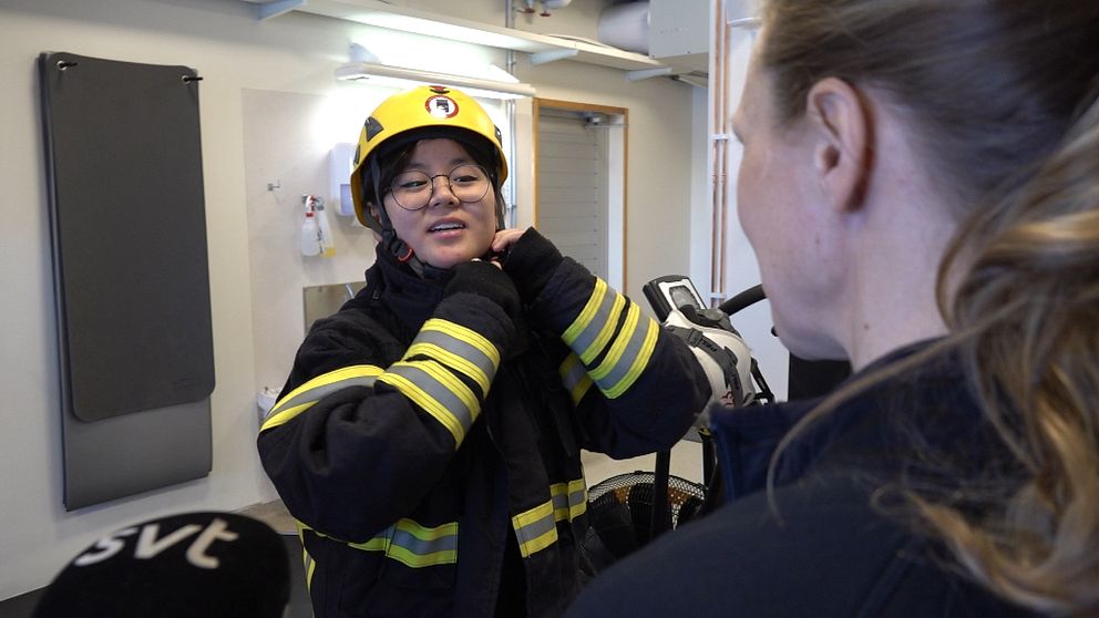 Isabella Wänman står i träningslokalen på brandstationen i Umeå, iklädd brandmanskläder och knäpper hjälmen för att göra rökdykarprovet.