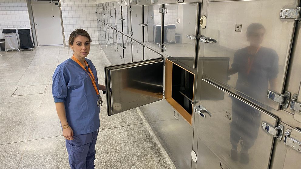 Bårhus kvinna står med öppet fack där döda kyls i väntan på obduktion.