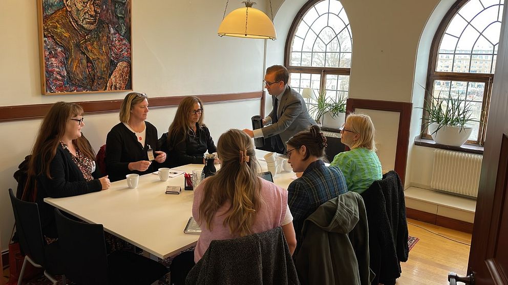 Sex kvinnor sitter samlade runt ett bord, socialborggarråd Alexander Ojanne (S) serverar kvinnorna kaffe.