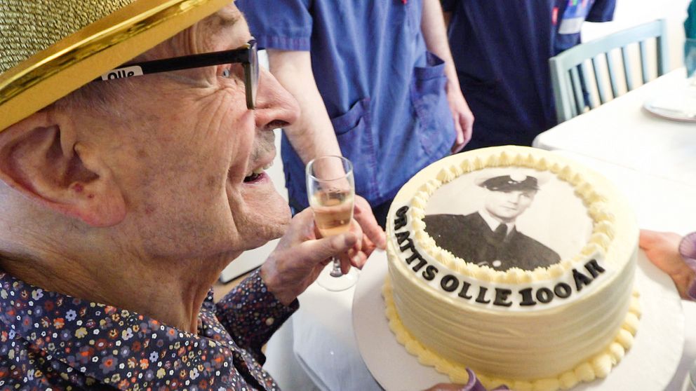 Olle Hernell med en partyhatt och en tårta där det står grattis olle 100 år.