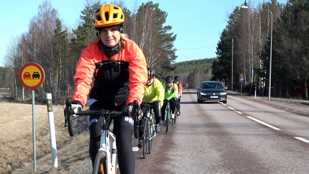 Cyklister som cyklar på landsväg, en bil kommer upp i bakgrunden