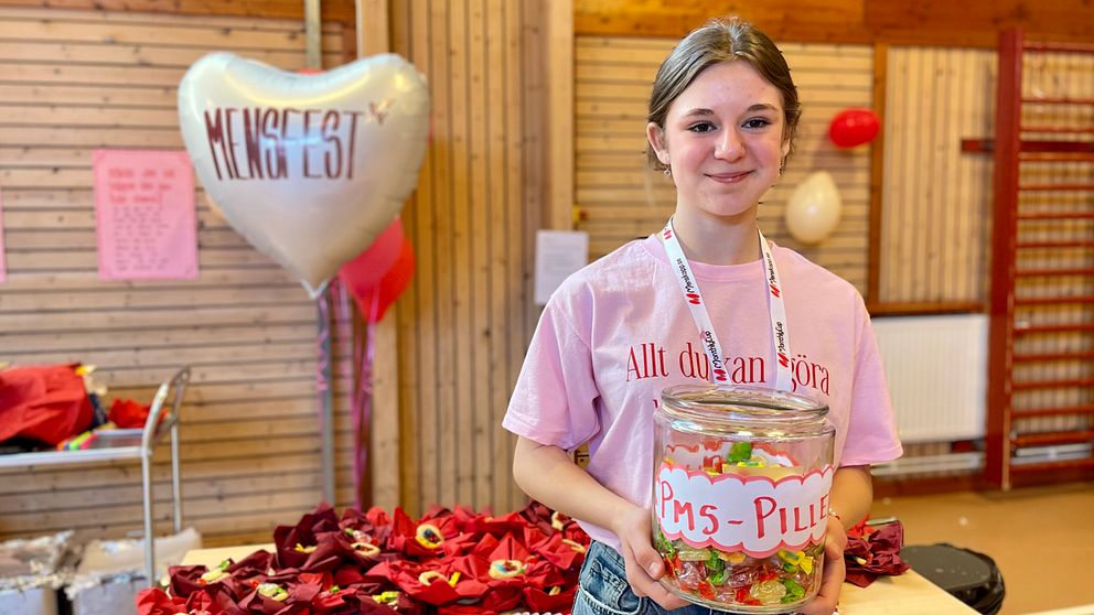 Otilia Clifford är en av initiativtagarna till Rönnbyskolans mensfest. Bakom henne på bordet ligger origamisnippor med snippkakor. Runt omkring i salen är det pyntat med ballonger. En ballong som är hjärtformat där står texten mensfest.