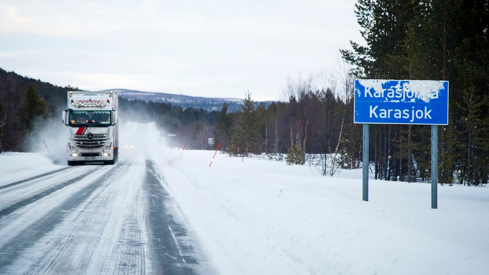 lastbil på en snåig väg vid infarten till Karasjok, vägskylt med ortnamnet till höger