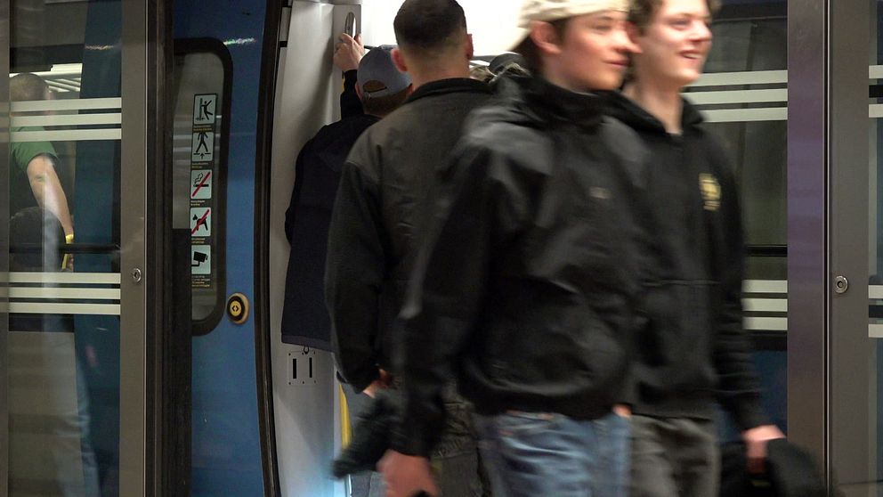 Bild på pendeltåg på station och resenärer som går in i tåget, dörren öppen.
