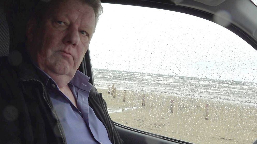 En man sitter i en bil. På bilrutan syns regndroppar.