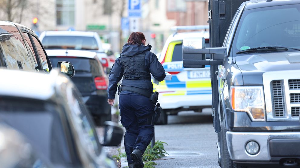 En kvinna i poliskläder går mellan bilar.