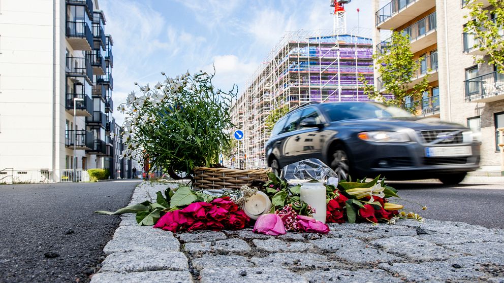 En bild på Långströmsgatan i Göteborg, där en bild passerar bakom flera blommor lagda på kullersten bredvid vägen.