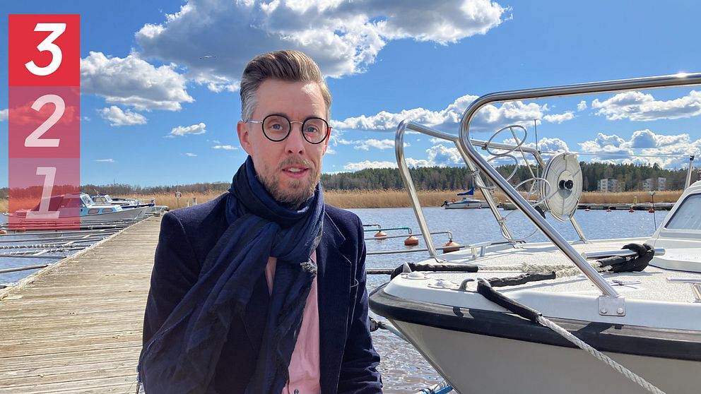 Man med glasögon och scarf i en båthamn, tittar in i kameran.