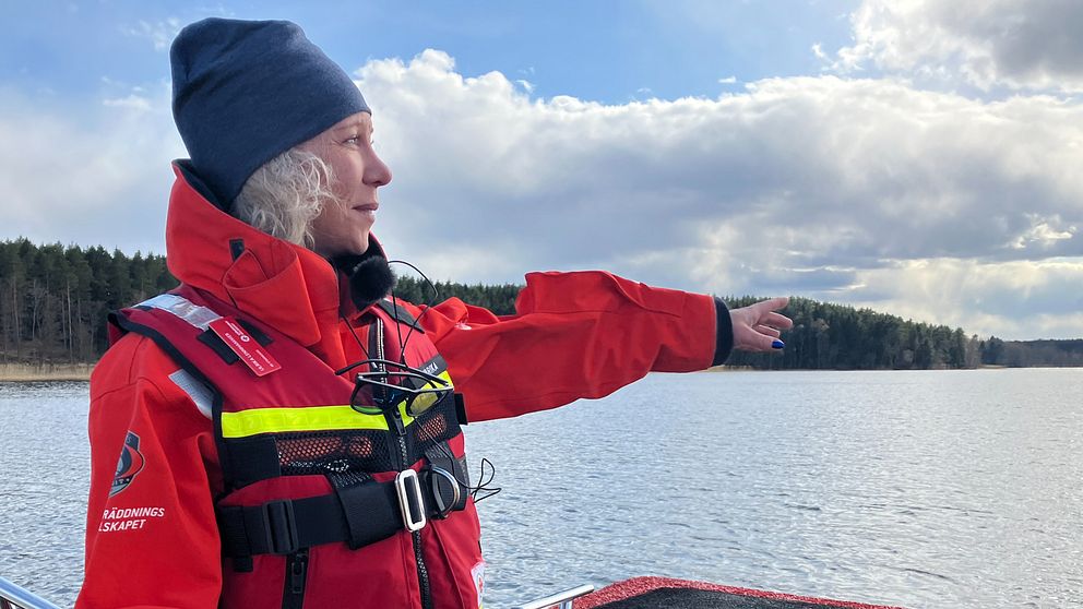 Kvinna med mössa, röd jacka och flytväst pekar ut från en båt.