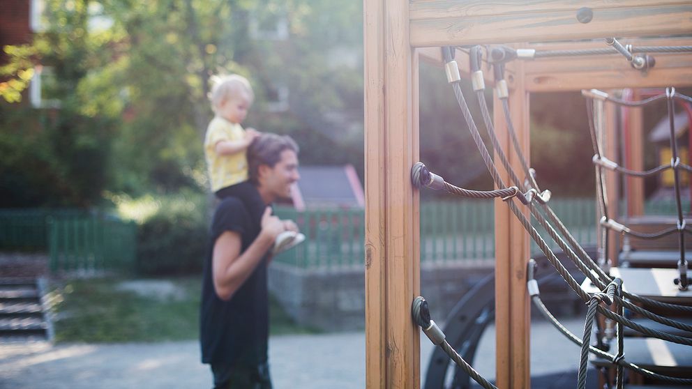 en pappa går med sitt barn på axlarna i en lekpark