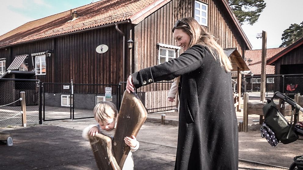 Emma Vikström står på en lekplats i Rättvik och leker med sin son. Hon har långt ljusbrunt hår och svart jacka.