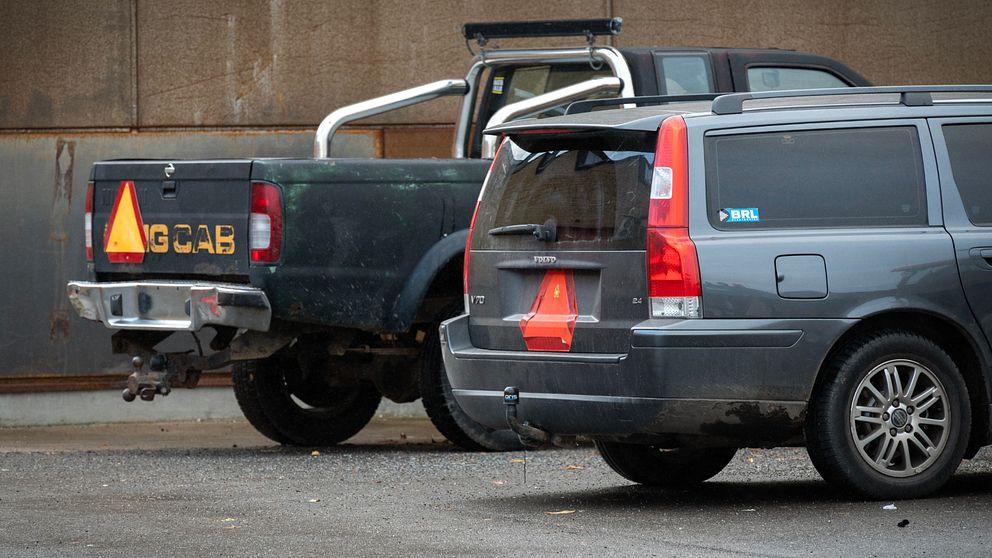 Två bilar med orange triangel på baksidan, står parkerade.