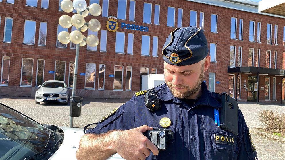en polis utanför polishuset i Borlänge. Han håller i en kroppskamera som sitter på hans uniform.