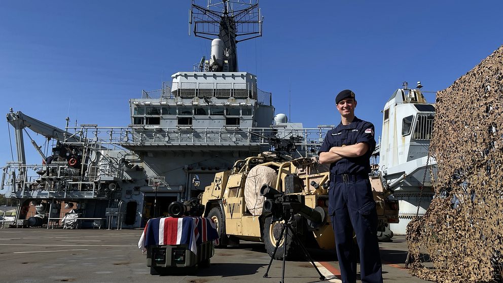 Fartygsserviceingenjören Tom Curtis står uppe på HMS Albions helikopterplatta som har plats för två helikoptrar samtidigt. På bilden syns också radarn, oilka vapen och den brittiska flaggan.