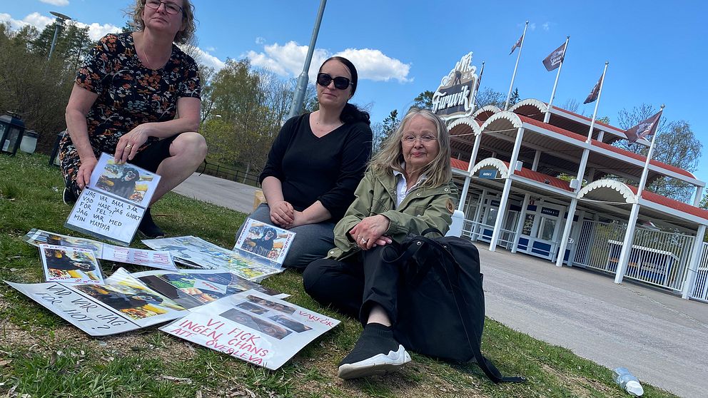 Tre kvinnliga demonstranter sitter framför Furuviks entré med sina plakat.