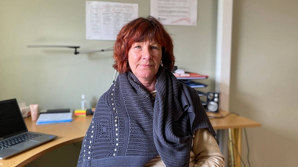 Annika Eriksson, stabschef i vård- och omsorgsförvaltningen, sitter på en stol vid en kontorsplats. Hon har en grå virkad sjal om axlarna och rödbrunt hår.