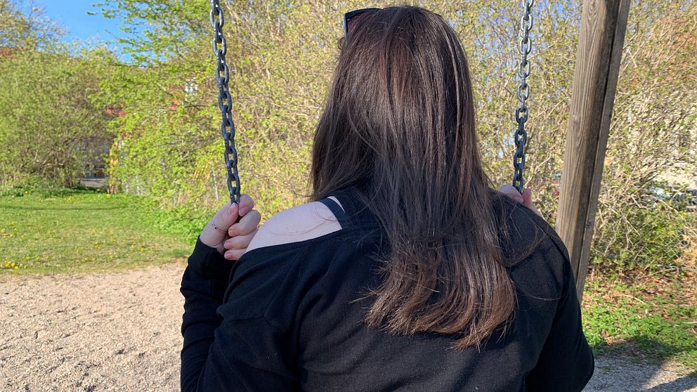 Anonym bild. En tjej i gymnasieålder med brunt hår sitter på en gunga. Bilden är tagen bakifrån så att man inte ser tjejens ansikte.