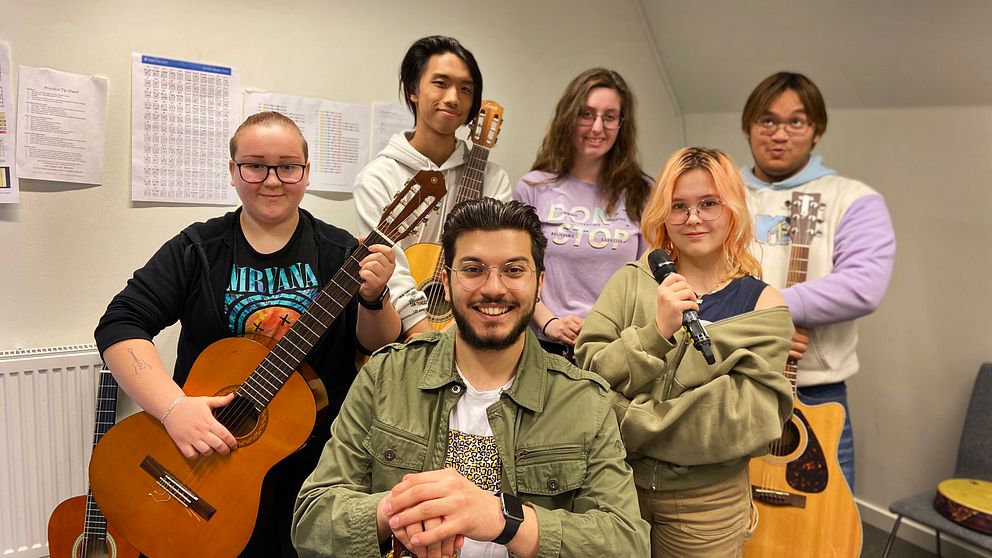 Sex bandmedlemmar av olika kön och åldrar tittar in i kameran med sina instrument.