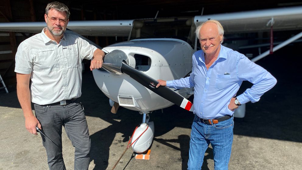 Två män håller i propellern längst fram på ett flygplan.