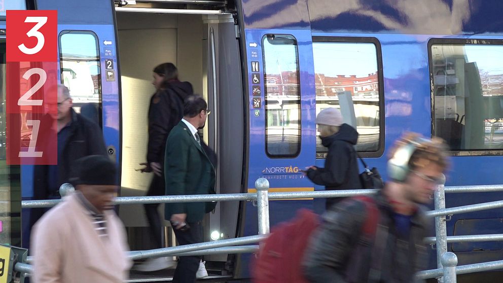 Ett blått tåg står på en perrong, människor går in och ut ur tåget.