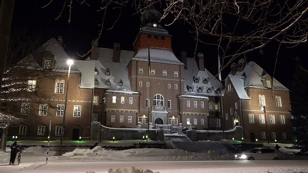 Östersunds rådhus, en stor tegelbyggnad. Det ligger snö på taken och på marken och huset är upplyst av lampor.