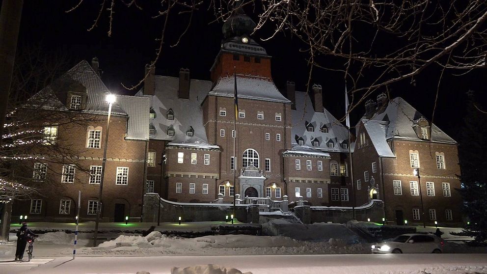 Östersunds rådhus, en stor tegelbyggnad. Det ligger snö på taken och på marken och huset är upplyst av lampor.