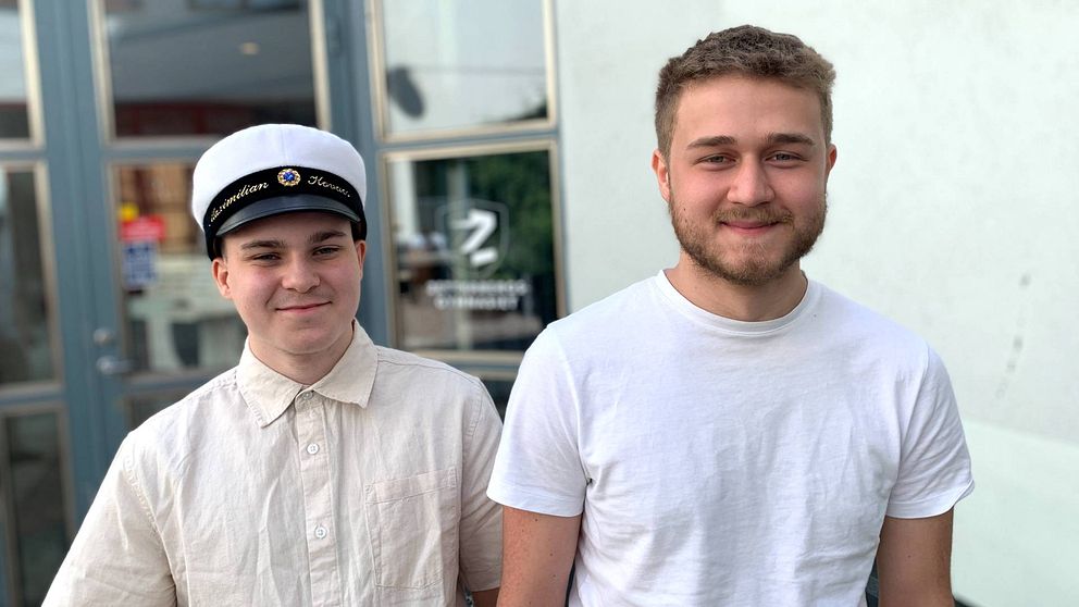 Två unga killar, en med studentmössa, ler mot kameran.