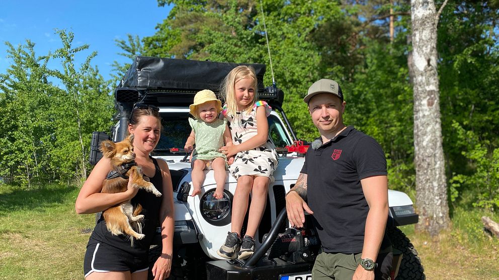 Familj som består av fyra personer och en hund står framför en bil med taktält.