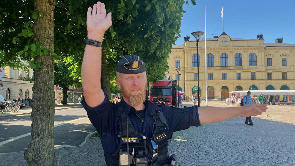 En polisman står med ena handen sträckt rakt över sitt huvud och den andra armen är utsträckt vid sidan.
