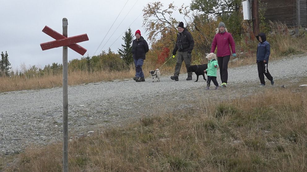 vuxna och barn med en hund på fjällvandring, i förgrunden ett rött kryss som markerar vandringsleden