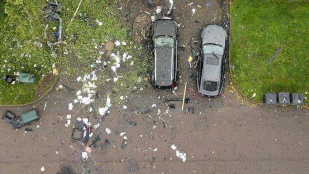 Två bilar står parkerade på en uppfart medan den tredje bilen har blivit till småskrot efter en explosion.