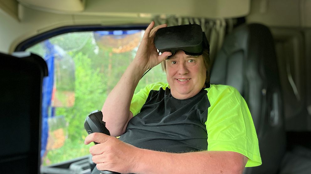 Thomas Bergander, man i svart och neongul t-shirt sitter i en lastbil med en joystick och ett par VR-glasögon i pannan.
