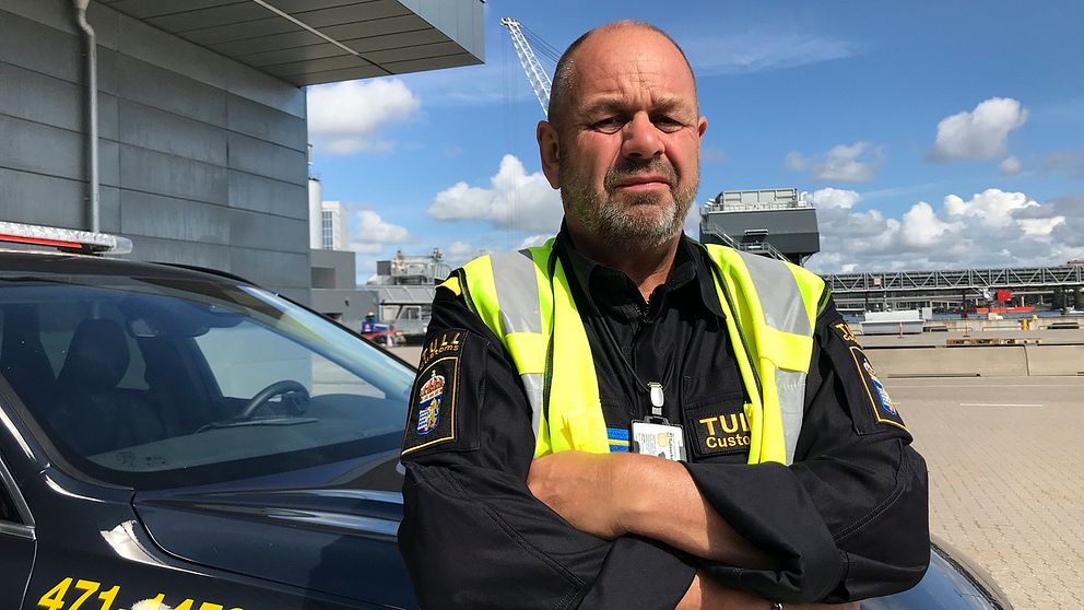 Johan Larsen på Tullverkets kontrollenhet Öst  står i hamnmiljö framför ett tullfordon.