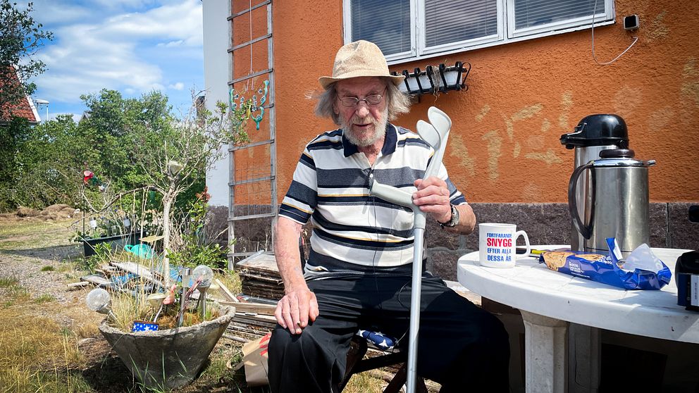 Billy Tapper sitter utomhus vid ett plastbord. Han håller en krycka i handen.